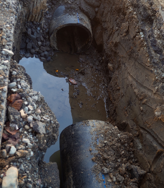 Intervention sur canalisation d’assainissement endommagée avec tranchée et écoulement d’eau.